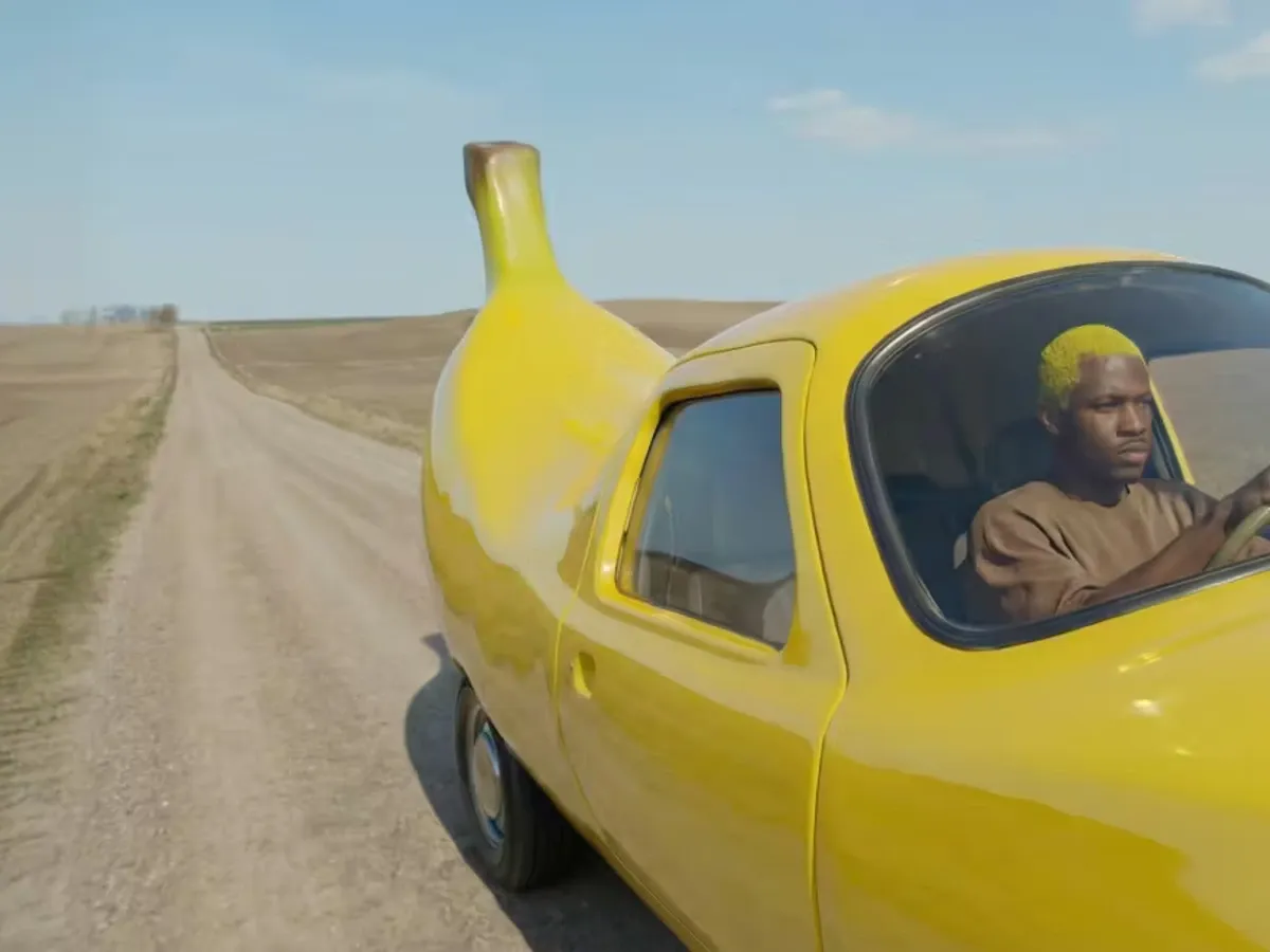Sample: a man drives a banana-shaped yellow car down a country road